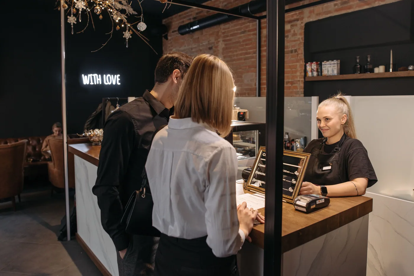 A café employee helping customers at the counter beside a payment terminal.